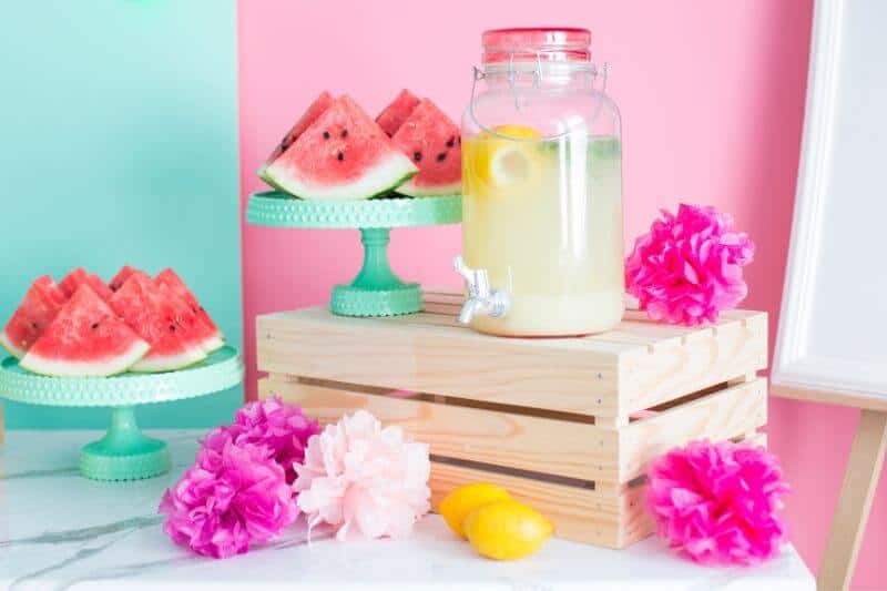 watermelon pieces, a lemonade tap and flower decorations on a table - Watermelon Party idea for summer
