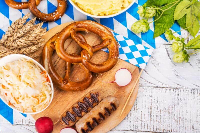 Oktoberfest party food like a big pretzel, salad and bratwurst on a wooden background.