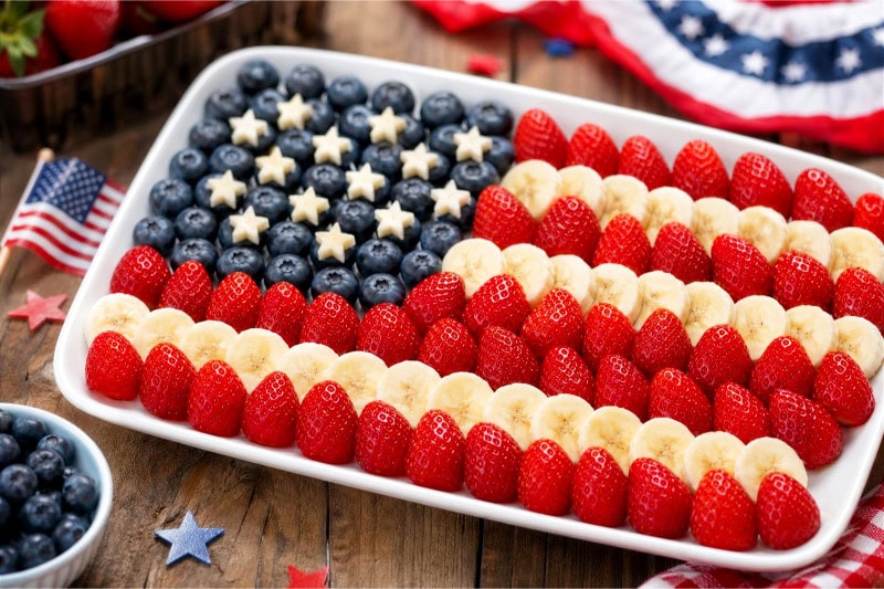 A fruit platter with strawberries, blueberries, and banana slices arranged to resemble the American flag on a wooden table.