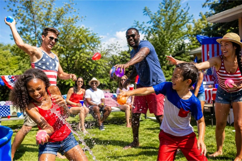 Children and adults happily tossing water balloons outdoors during a summer party.