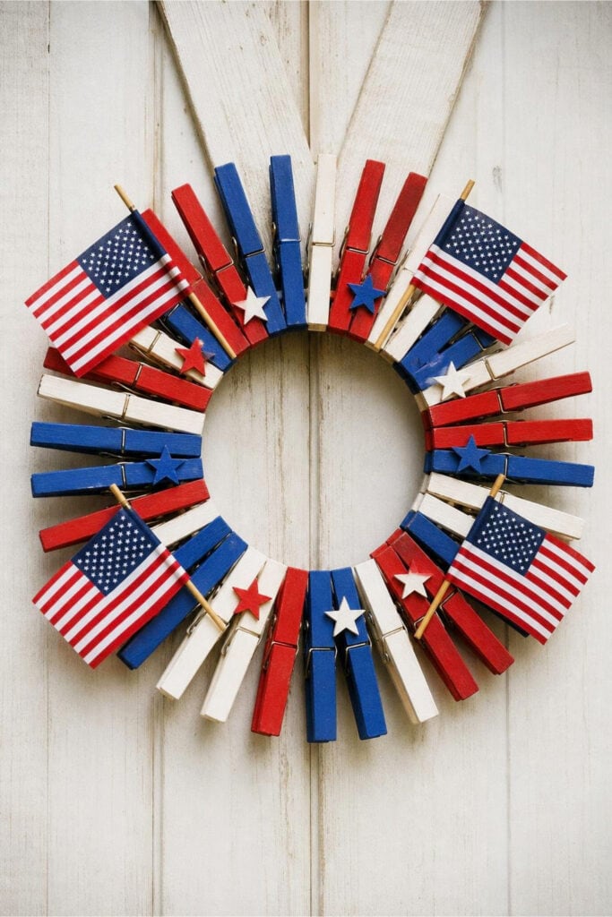 A colorful clothespin wreath decorated with small American flags hanging on a wooden door.