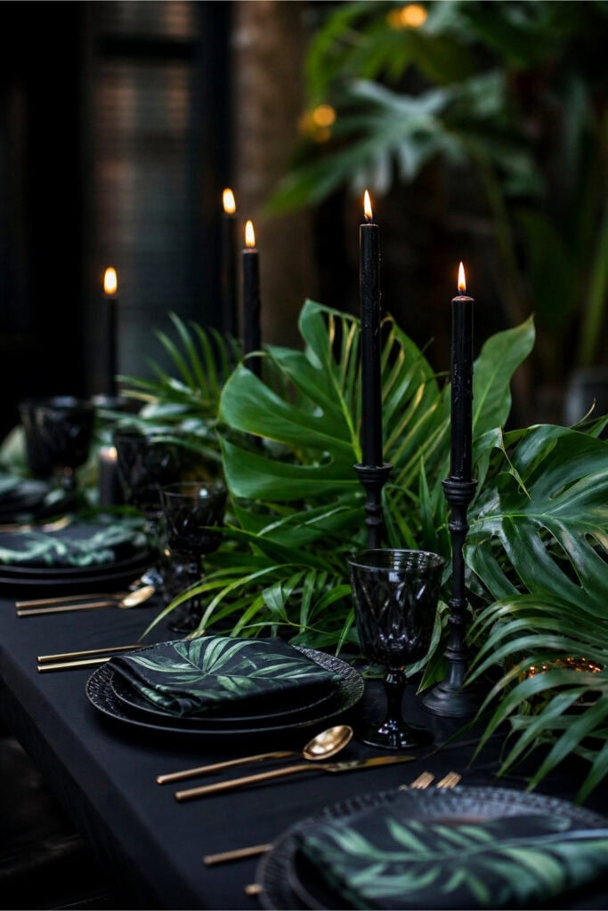 A table decorated with black candles and tropical green leaves arranged for a summer party.