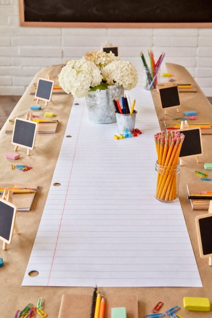 A table covered with kraft paper and a notebook paper table runner, decorated with school supplies and party items.
