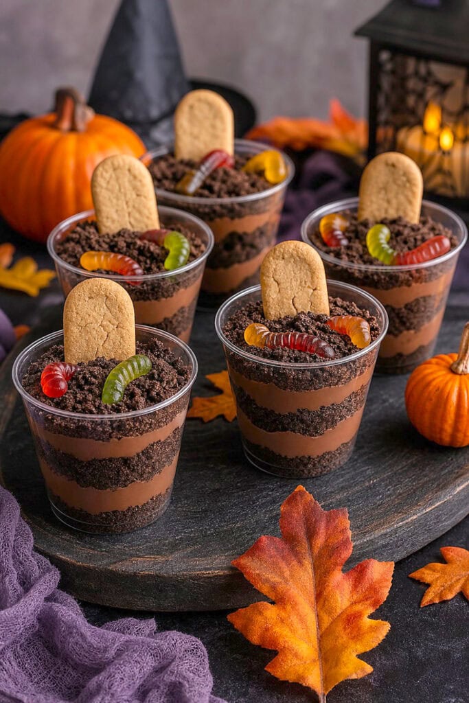 Individual chocolate pudding cups decorated like miniature Halloween graveyards with cookie tombstones and gummy worms.