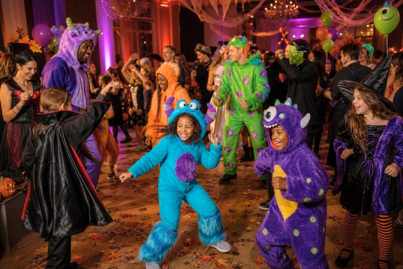 A diverse group of people in friendly monster costumes dancing at a festive Halloween party.